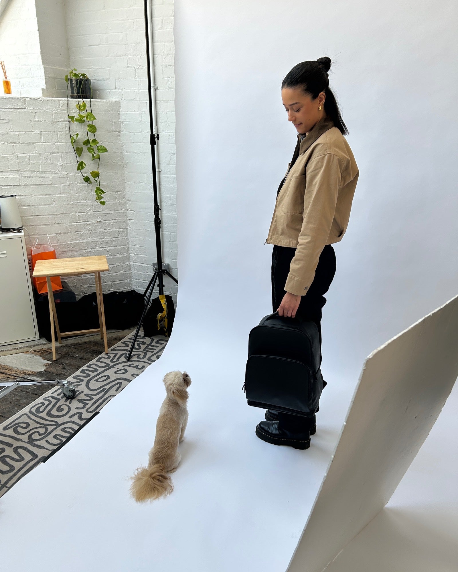 Behind the scenes of the Fetchamo studio photoshoot with the model holding the Core Backpack while looking at a Shih Tzu on set.