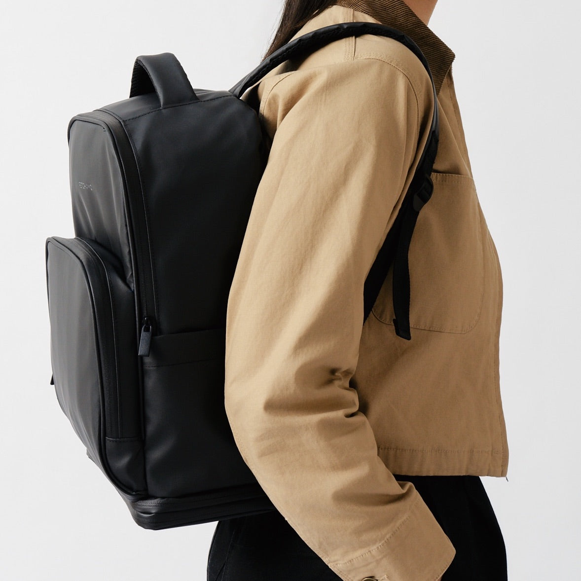 Side profile of a model wearing the black Fetchamo Core Backpack in a studio, highlighting its structured silhouette and minimalist design.