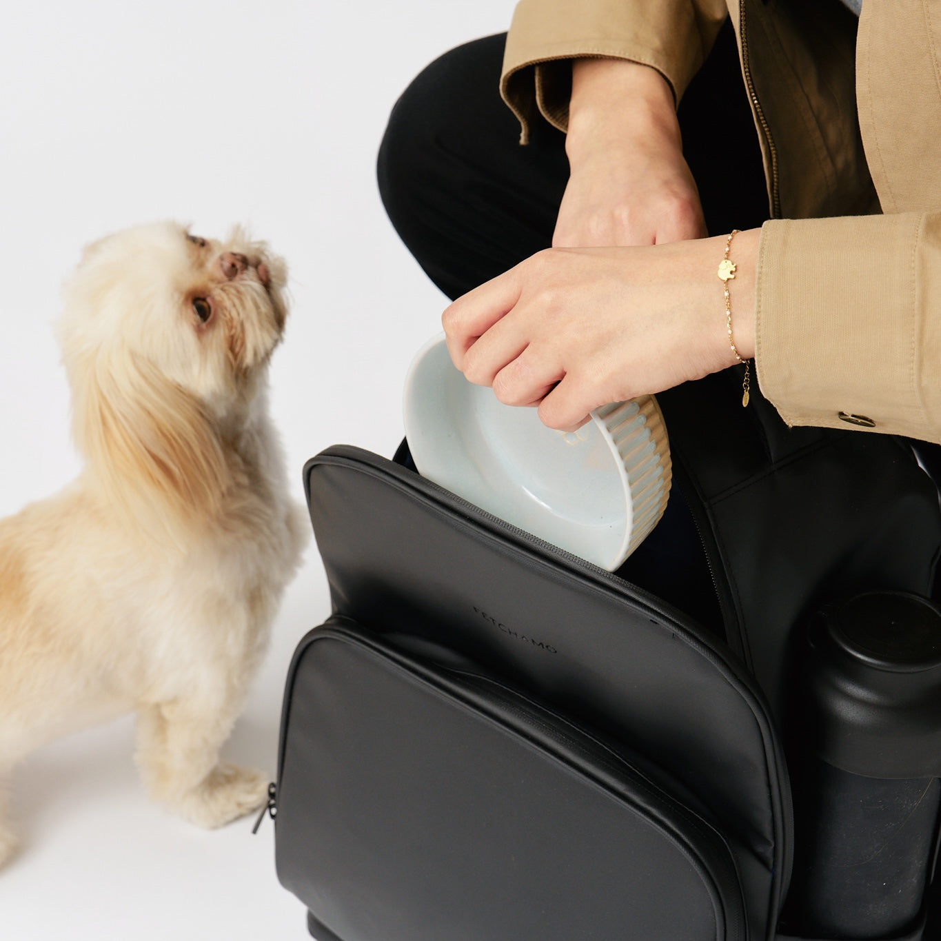fetchamo Core backpack for dog owners – model placing a dog bowl into the backpack with dog beside her