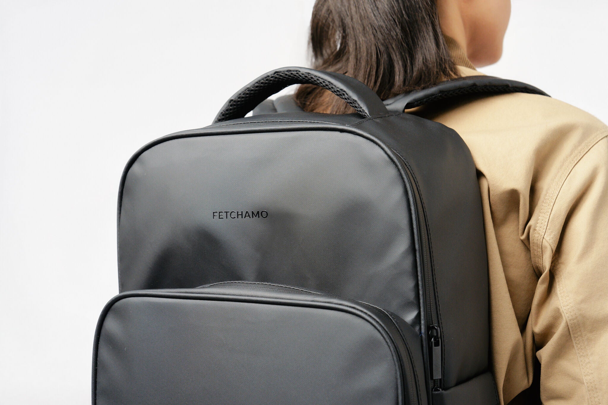 Rear view of a model wearing the black Fetchamo Core Backpack in a studio, showcasing the structured design and front logo.